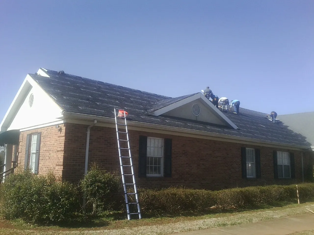 Crew tearing shingles off a brick ranch roof with a ladder set — Metal Roof Repair work by our crew in Tremonton
