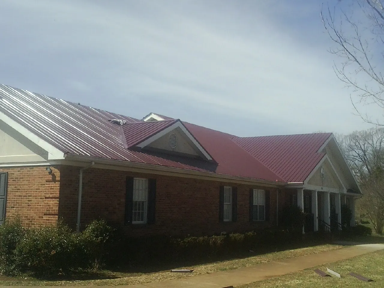 Red metal roof with gabled entries on a long brick building, from a Hail Damage Roof Repair job in Tremonton