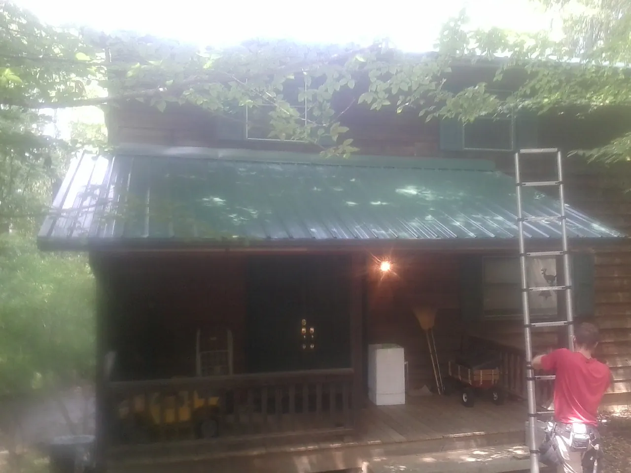 Worker on a ladder at the green porch roof of a wooded cabin in Tremonton