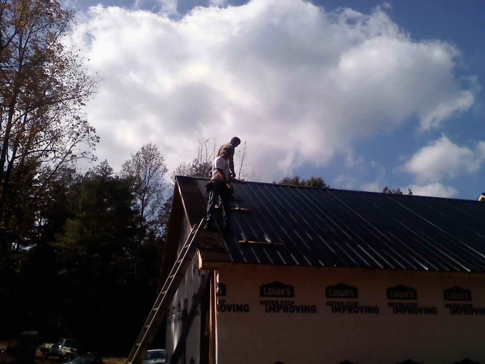 Roofer fastening dark metal panels high against a cloudy sky, from a Roof Inspection job in Tremonton