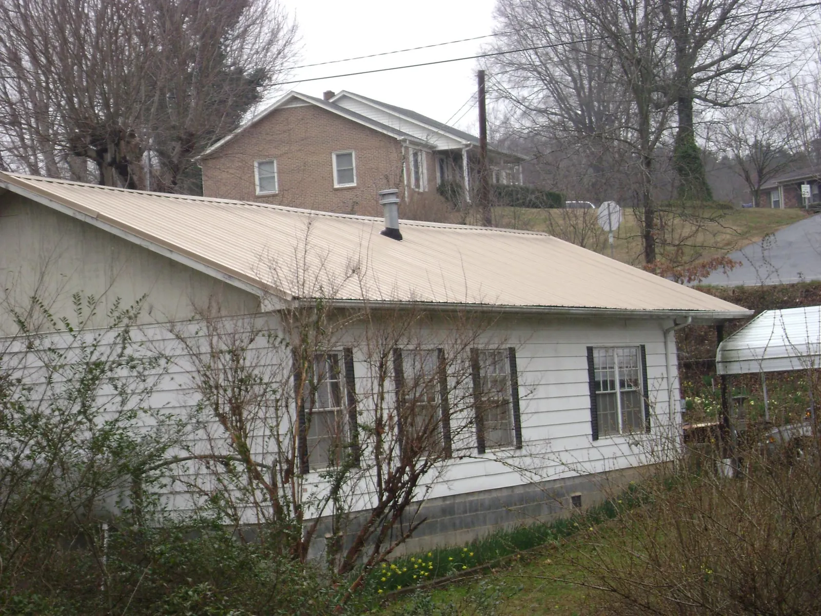 Tan metal roof on a white sided house set into a hillside — Commercial Roofing by Roofing Brothers in Tremonton