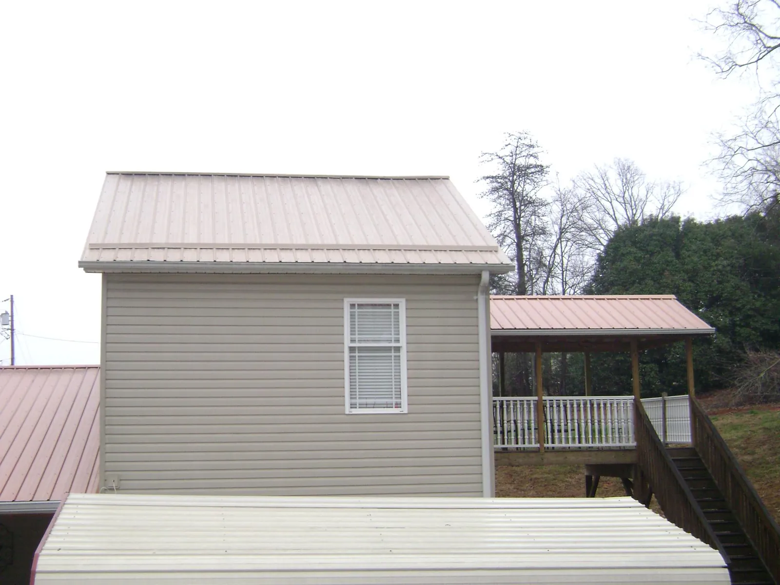 Tan metal roofs on a two story addition and attached porch, from a Roof Replacement job in Tremonton